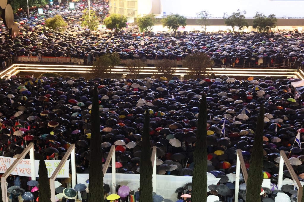 Protesters huddle under umbrellas at rally against Prime Minister Benjamin Netanyahu's new hard-right government in Tel Aviv on 14 January (AFP)