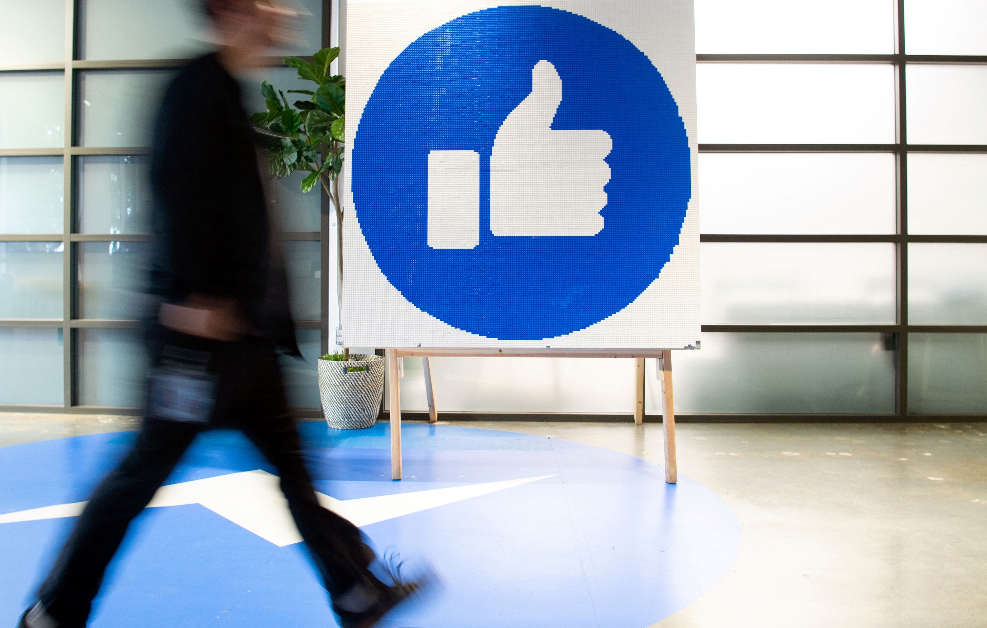 a Facebook employee walking past a sign displaying the "like" sign at Facebook's 