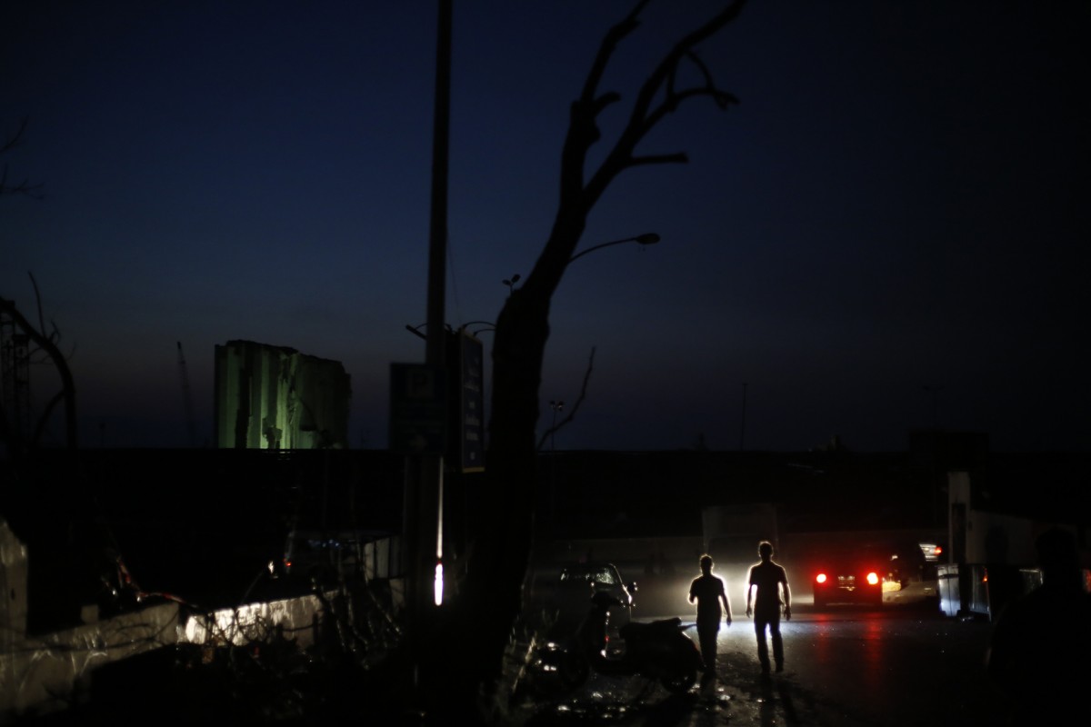 In a pitch-black Mar Mikhail neighbourhood, pedestrians are silhouetted by headlights and the green flood lamps of international rescue teams (Marwan Tahtah)