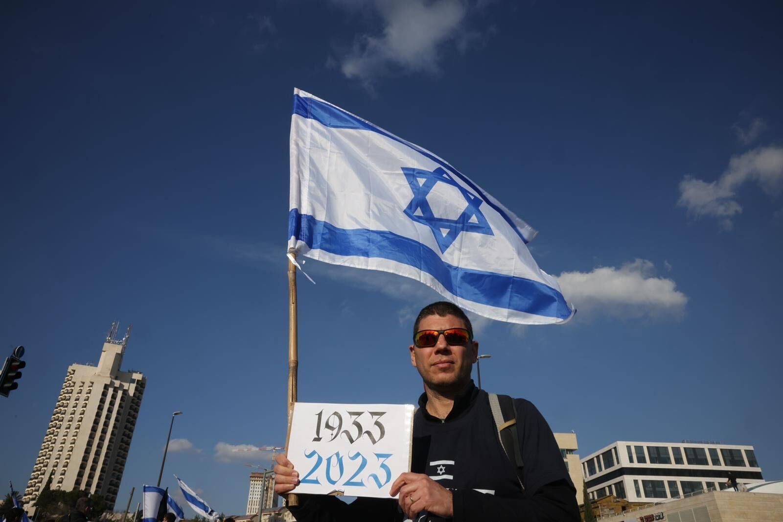 An Israeli protester holds up a sign comparing the rise of authoritarianism in Germany to that in Israel, on 13 February, 2023 (MEE)