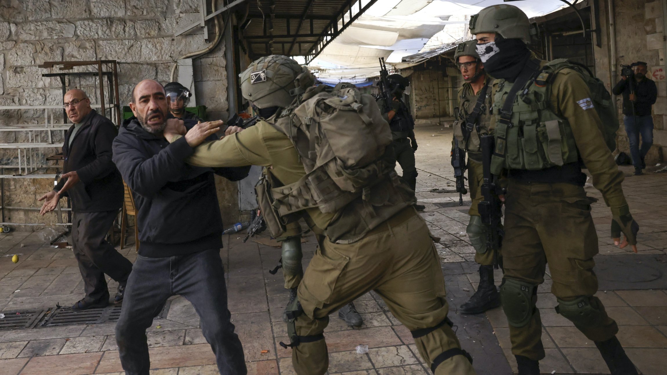 Israeli security forces hold back a Palestinian man, as Jewish settlers march in the occupied West Bank city of Hebron, on 19 November 2022 (AFP)