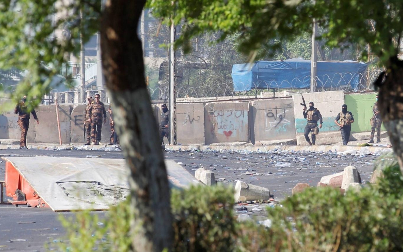 Un groupe d’hommes armés est visible près de la barrière de béton qui empêche toute progression vers la place Tahrir, à Bagdad, le 4 octobre 2019 (Reuters)