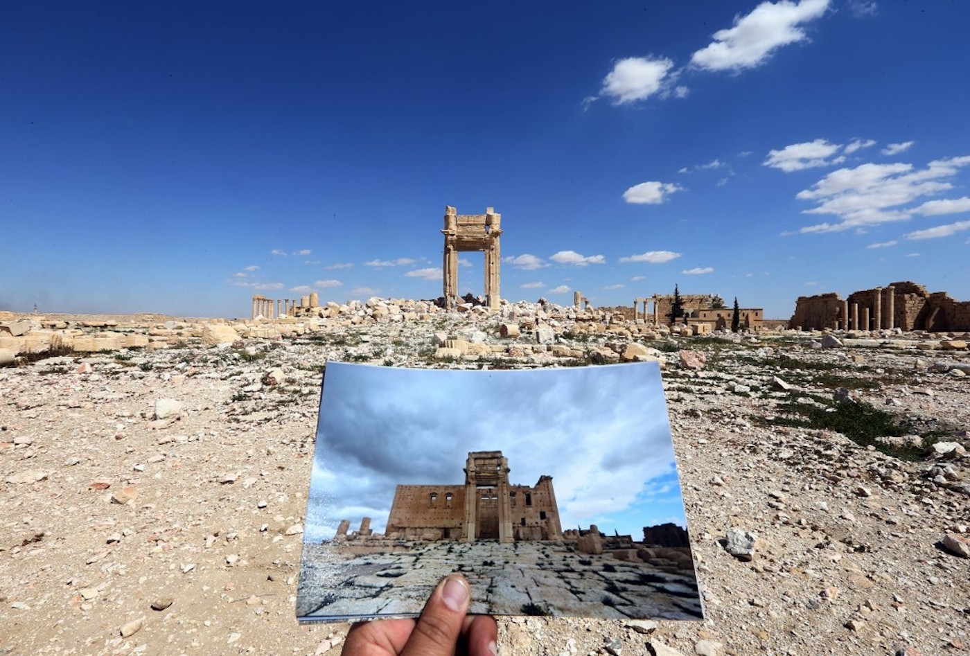 Une vue générale prise le 31 mars 2016 montre un photographe tenant un cliché du temple de Bêl de Palmyre,  le 14 mars 2014, devant les vestiges du temple historique après sa destruction par le groupe État islamique en septembre 2015, AFP