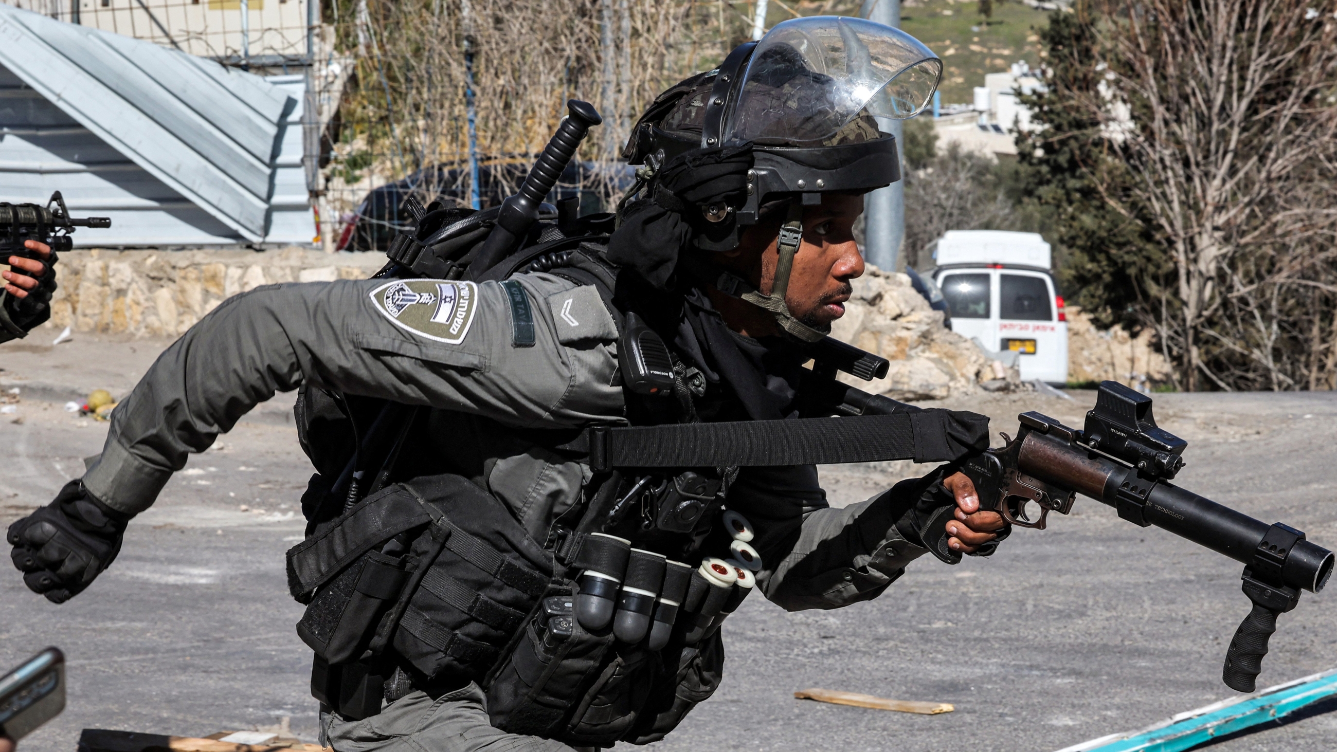 An Israeli officer runs with a riot-control gun during confrontations with Palestinians in Issawiya neighbourhood amidst a general strike declared in occupied East Jerusalem on 19 February 2023 (AFP)