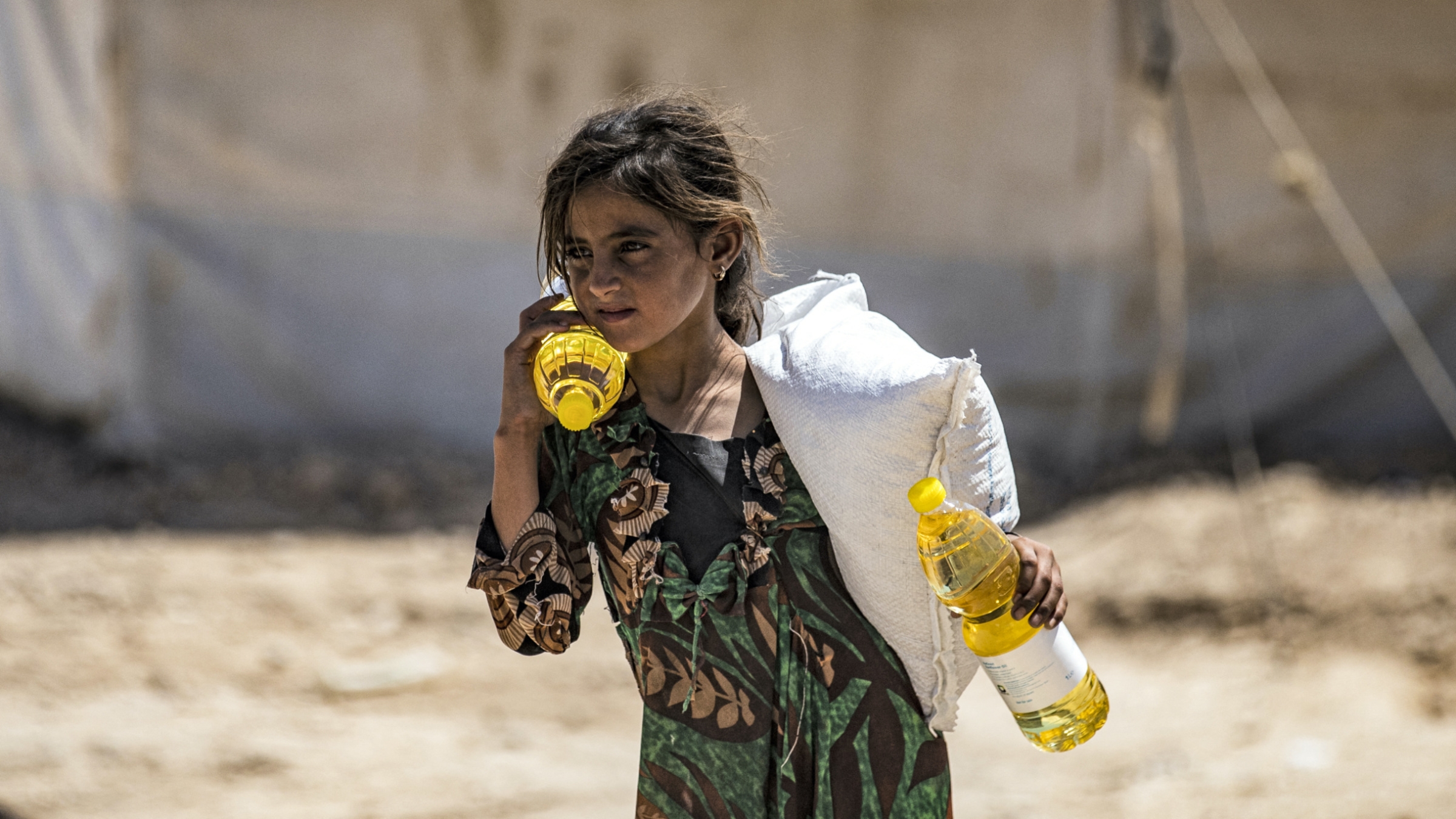 A girls walks carrying bottles of cooking oil at the Kurdish-run al-Hol camp in Syria's northeastern Hasakah province on 18 August 2021 (AFP)