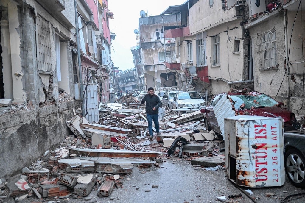 A man runs along a street strewn with debris, in Hatay, southern Turkey, on 7 February, 2023 (AFP)